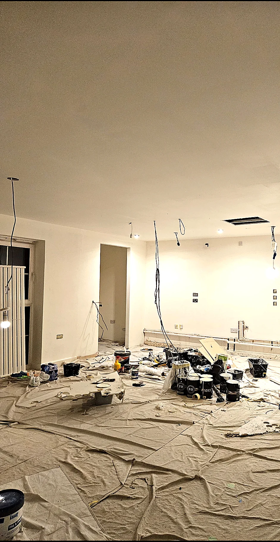 Room during refurbishment with ceiling cable drops, plastered walls and protected floor
