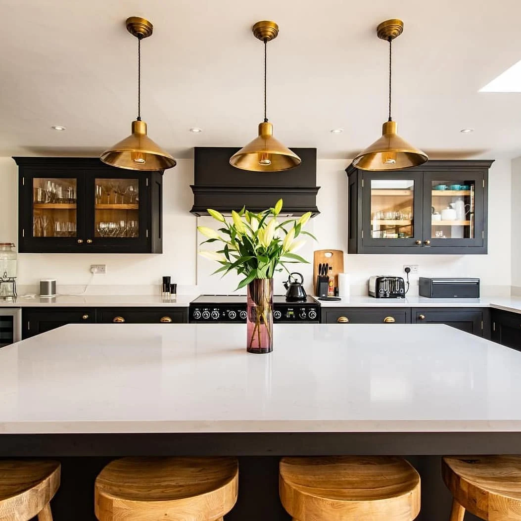 Black kitchen cabinetry with three brass pendant lights above a white island