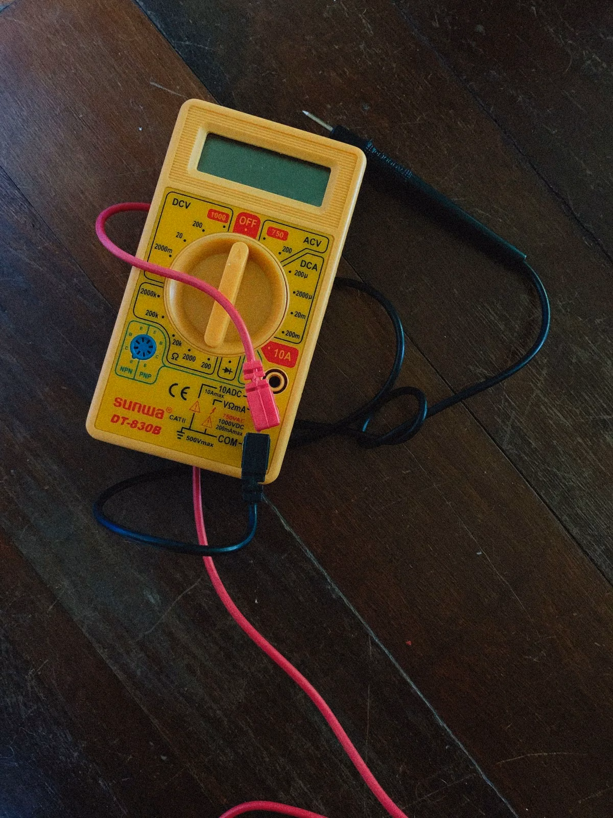 Digital multimeter and test leads resting on a wooden work surface