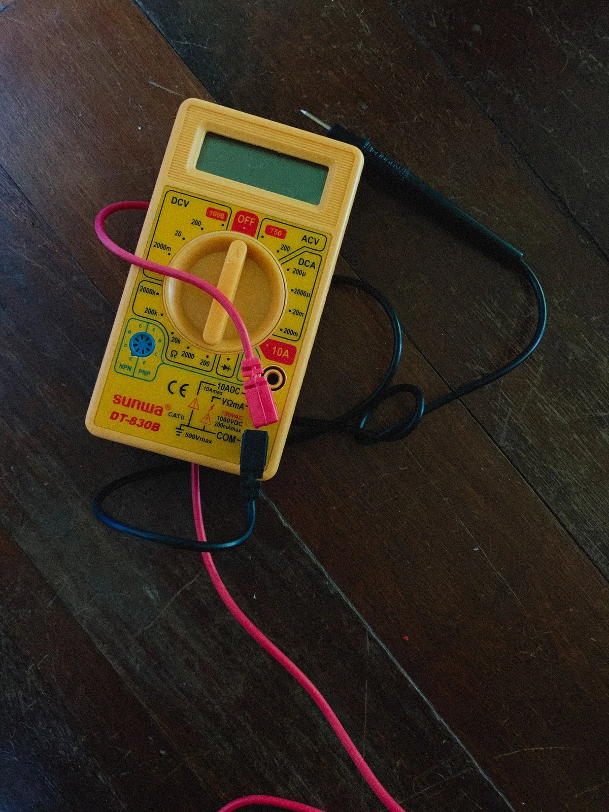 Digital multimeter and test leads resting on a wooden work surface